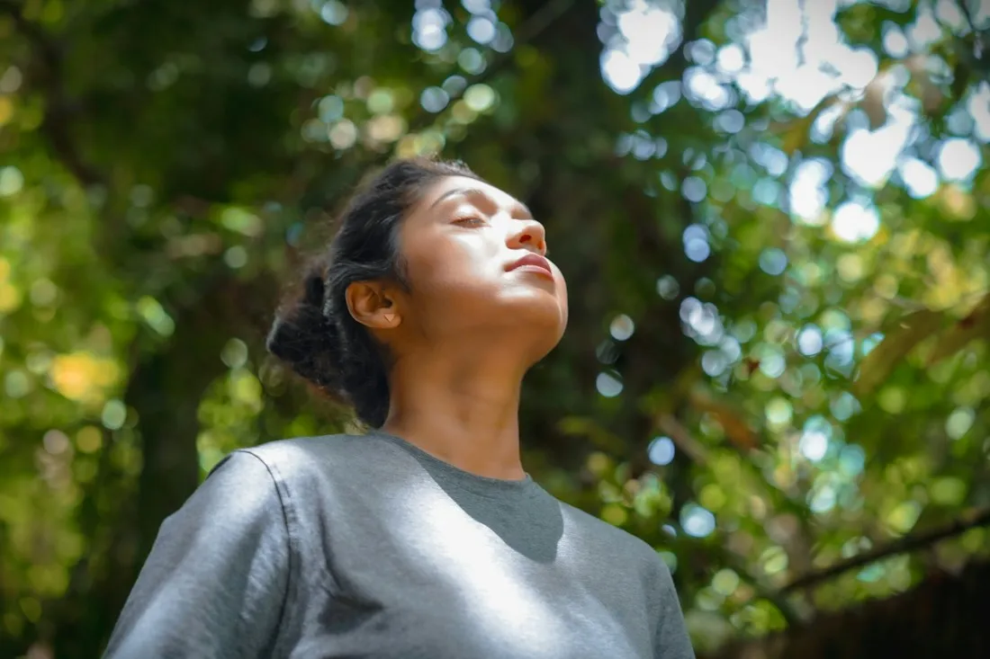 Woman with closed eyes taking a slow, deep breath under green trees for anxiety relief