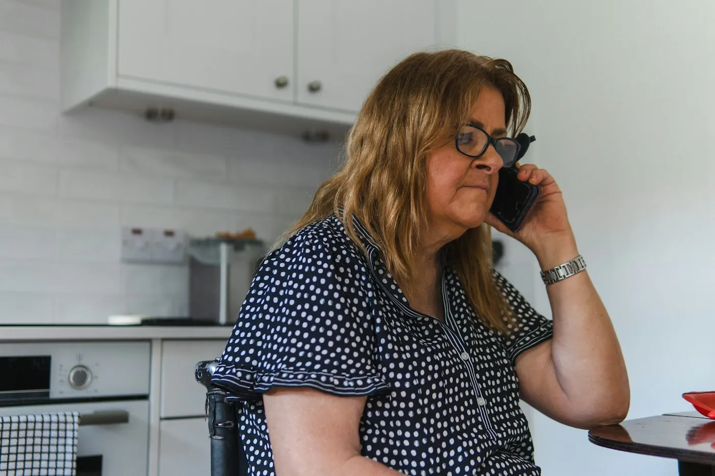 Woman sitting at her kitchen table talking on the phone with a support helpline