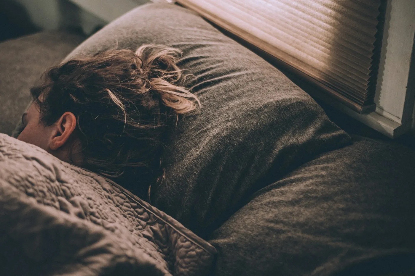 Woman sleeping soundly under a soft blanket in dim morning light, showing how sleep affects mental health
