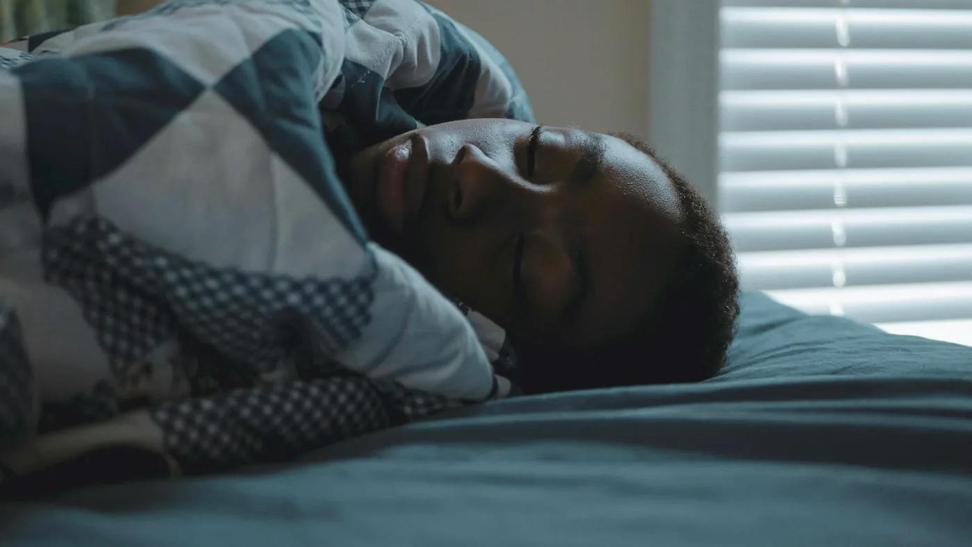Man sleeping peacefully under a patterned quilt in soft morning light after a calm night