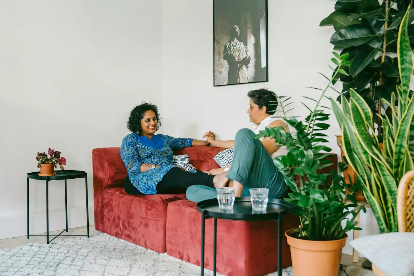 Two women sitting close on a sofa and holding hands during a supportive conversation at home