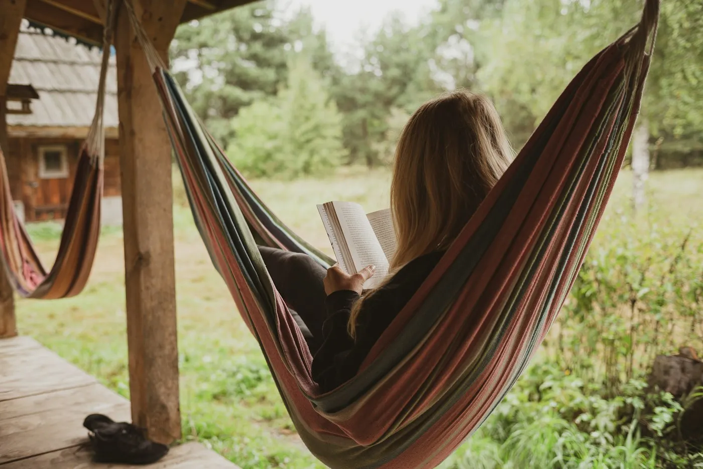 Woman reading a book while resting in a striped hammock outdoors, taking time to recover from burnout