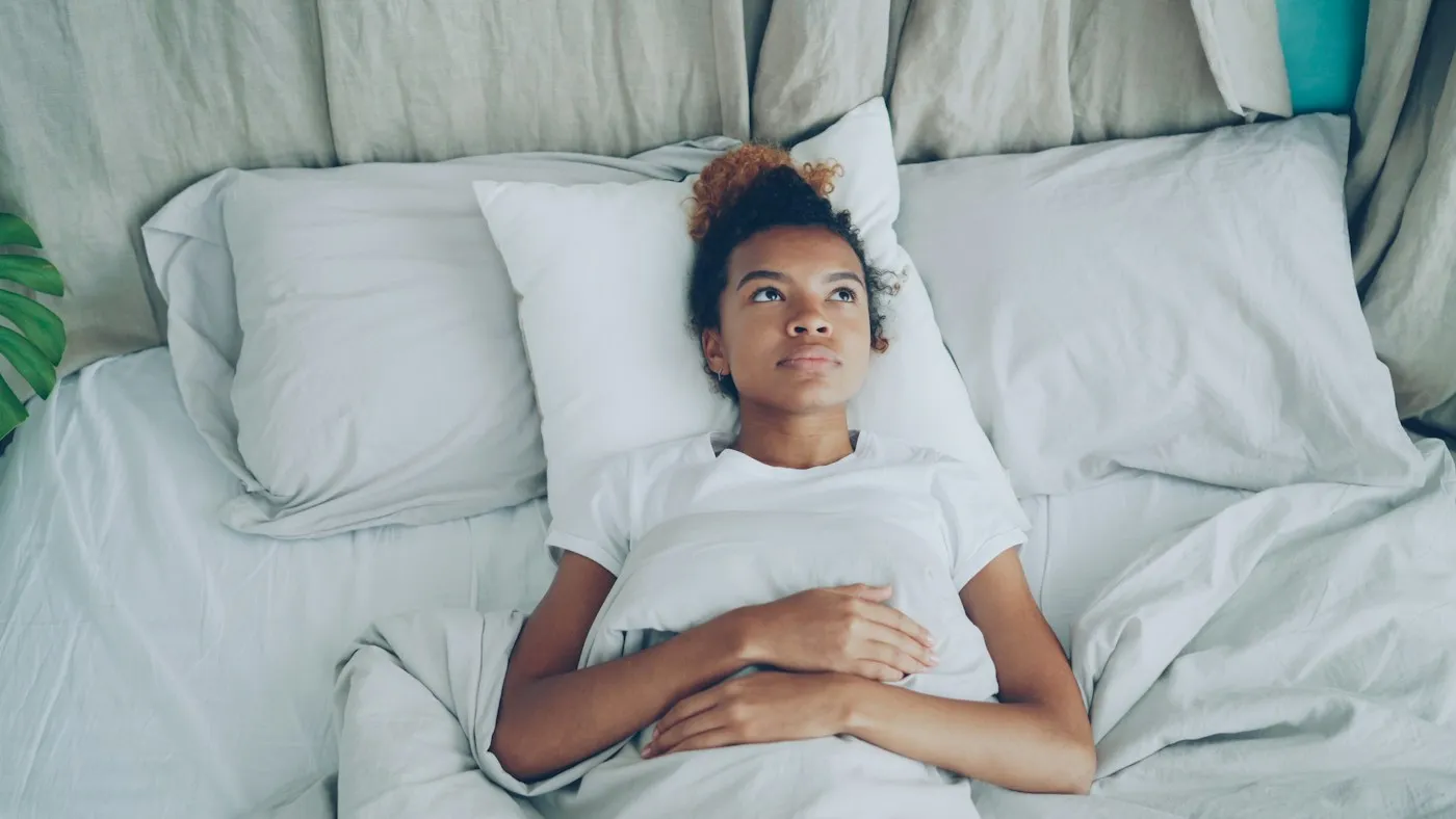 Young woman lying awake in bed with her hands resting on her stomach, dealing with racing thoughts at night