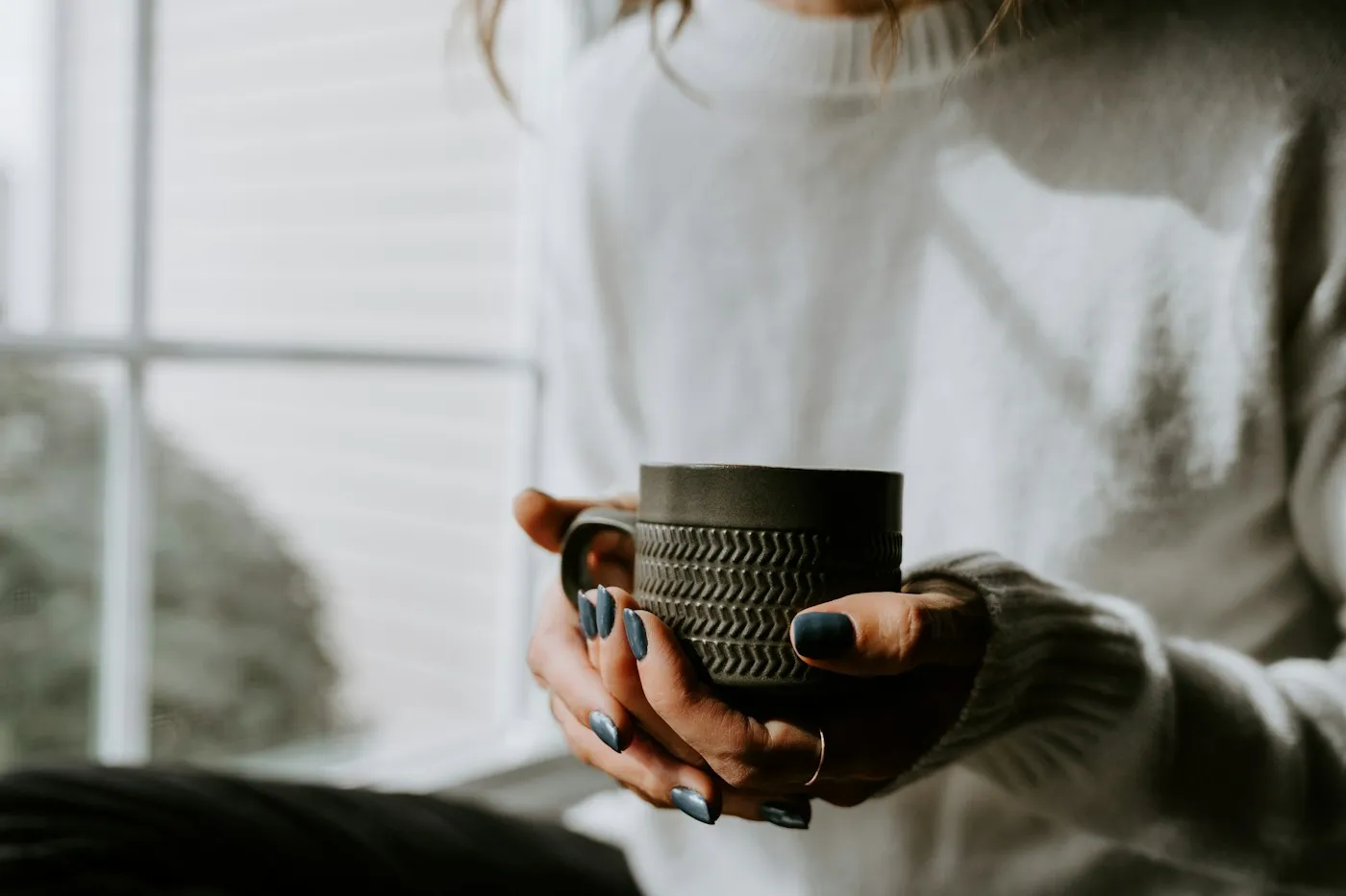Close-up of hands holding a warm ceramic mug by a bright window during a quiet mindful moment