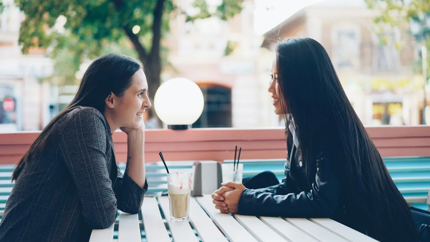 Two women having a calm, honest conversation at an outdoor cafe table, a relaxed setting for setting healthy boundaries