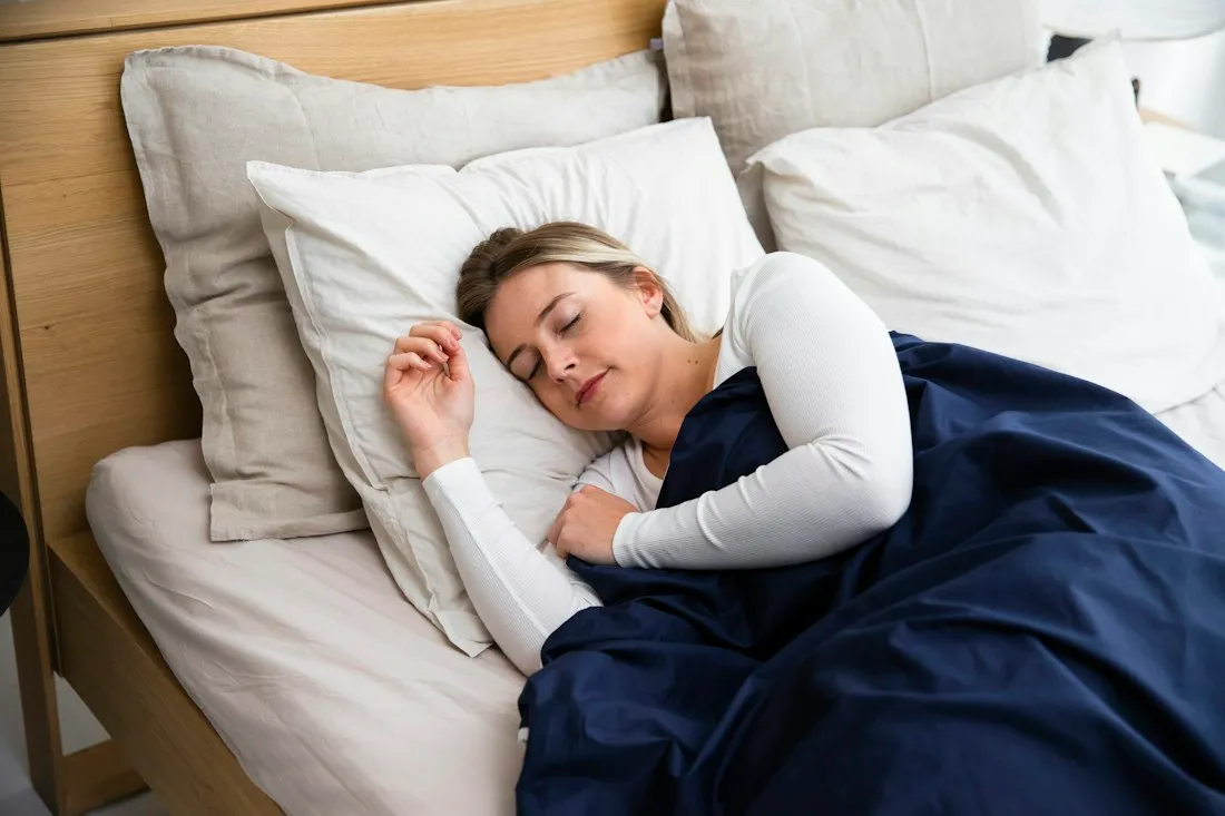 Woman sleeping peacefully in a bright bedroom, showing the link between restful sleep and mental health