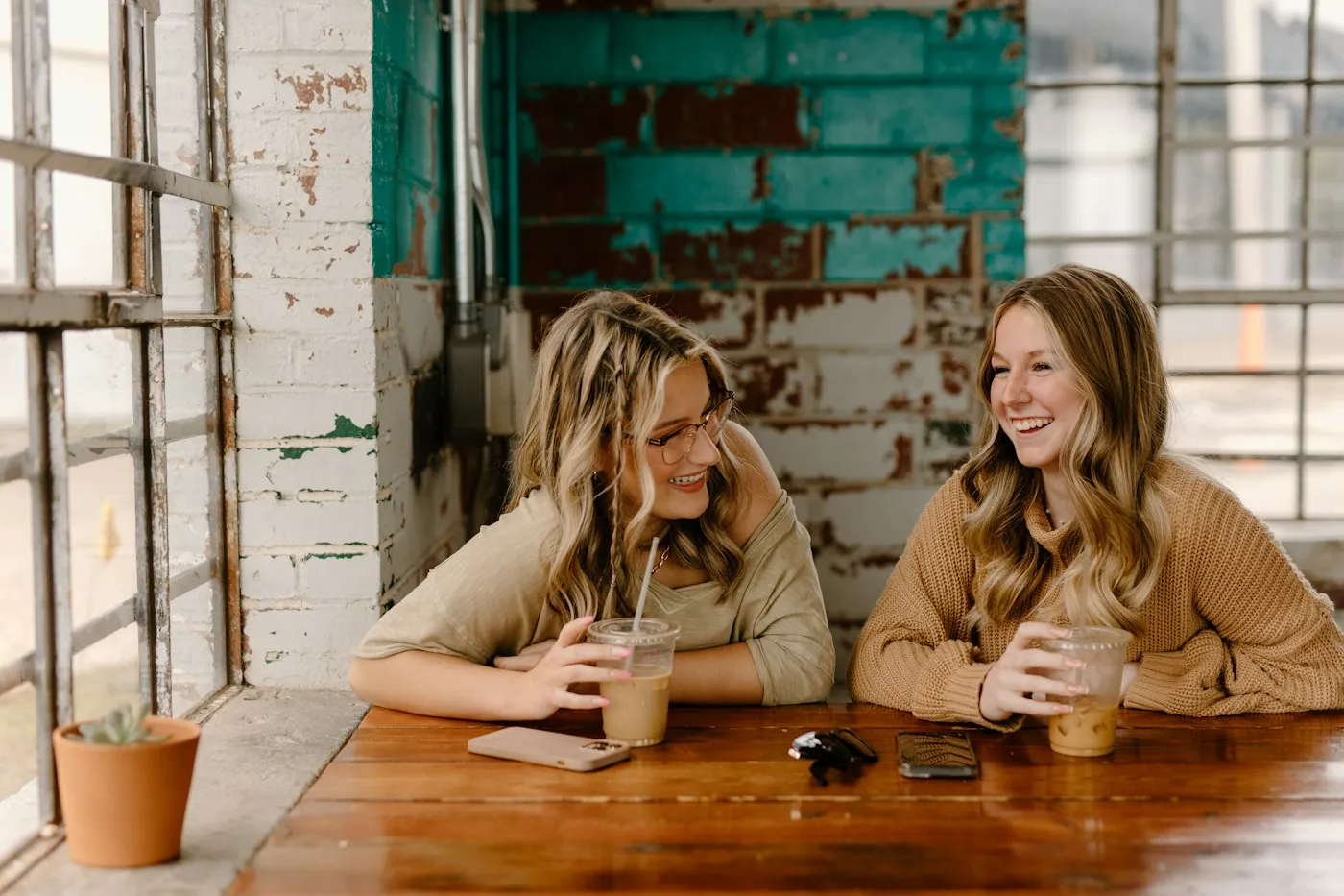 Two friends laughing and chatting over iced coffee at a bright cafe table