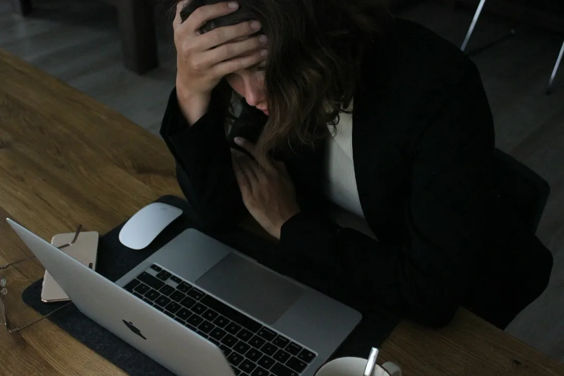 Tired woman holding her head in one hand while working late at a laptop, a common picture of stress and burnout